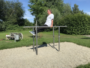 s'entraîne sur le playfit Barres parallèles K05005 dans un parc avec surface en gravier